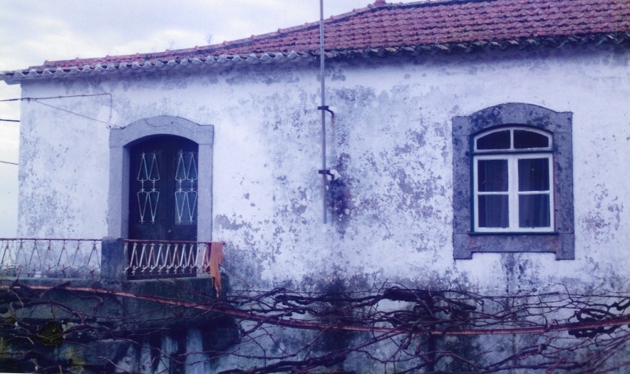 Fotografia antiga do terreiro da casa, com a fachada por rebocar e a varanda em ferro
