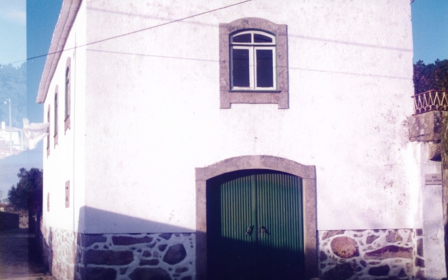 Fotografia antiga da empena da casa com portão de madeira verde e embasamento em pedra