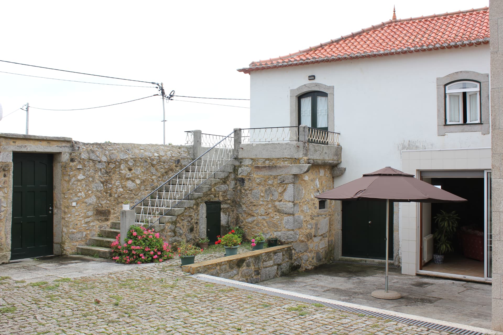 Pátio calcetado da Casa Praia e Campo com guarda-sol aberto e escadaria de granito