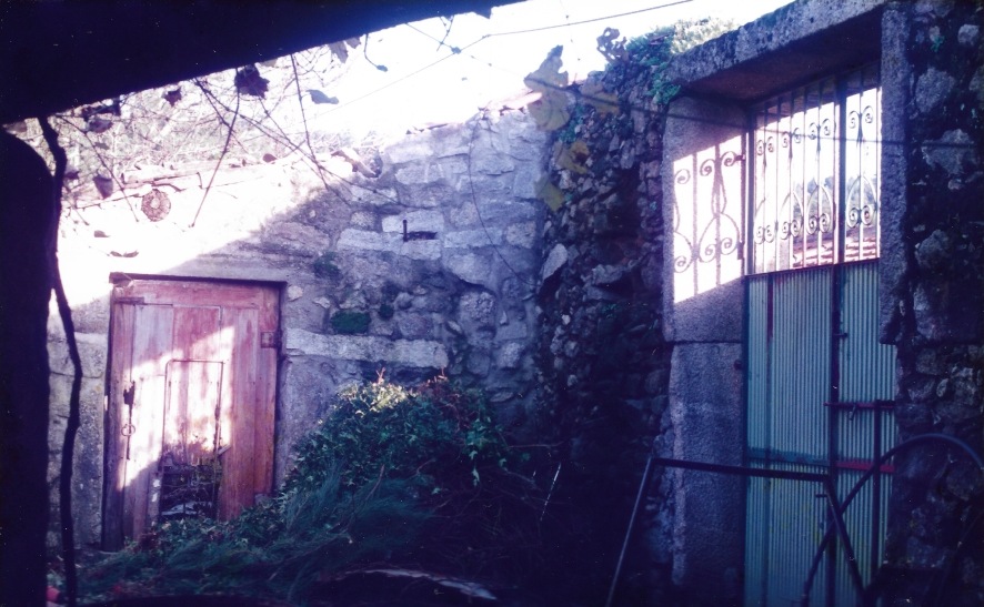 Fotografia antiga do quinteiro com portas de madeira gastas e muros de pedra cobertos de vegetação