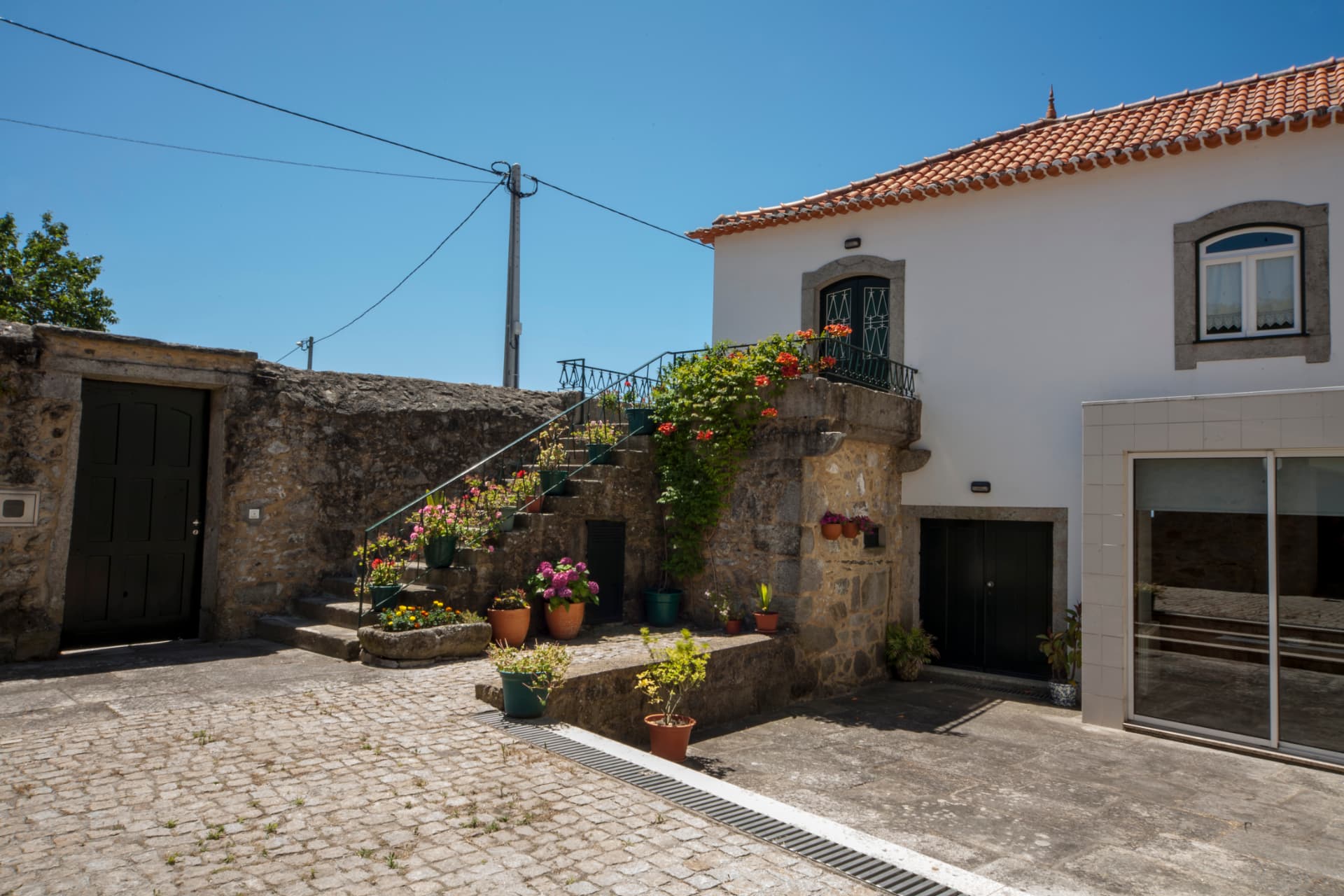 Pátio calcetado da casa com escadaria de granito florida e vasos de sardinheiras